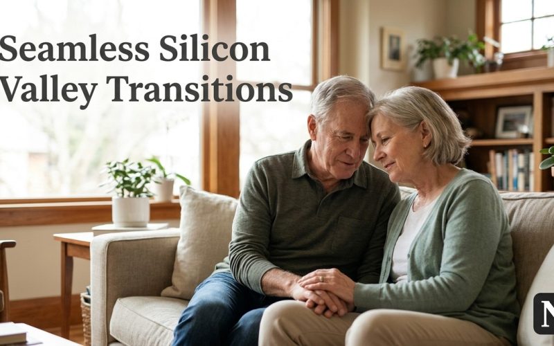 A senior couple sits on a couch, holding hands, with a window and bookshelf in the background.