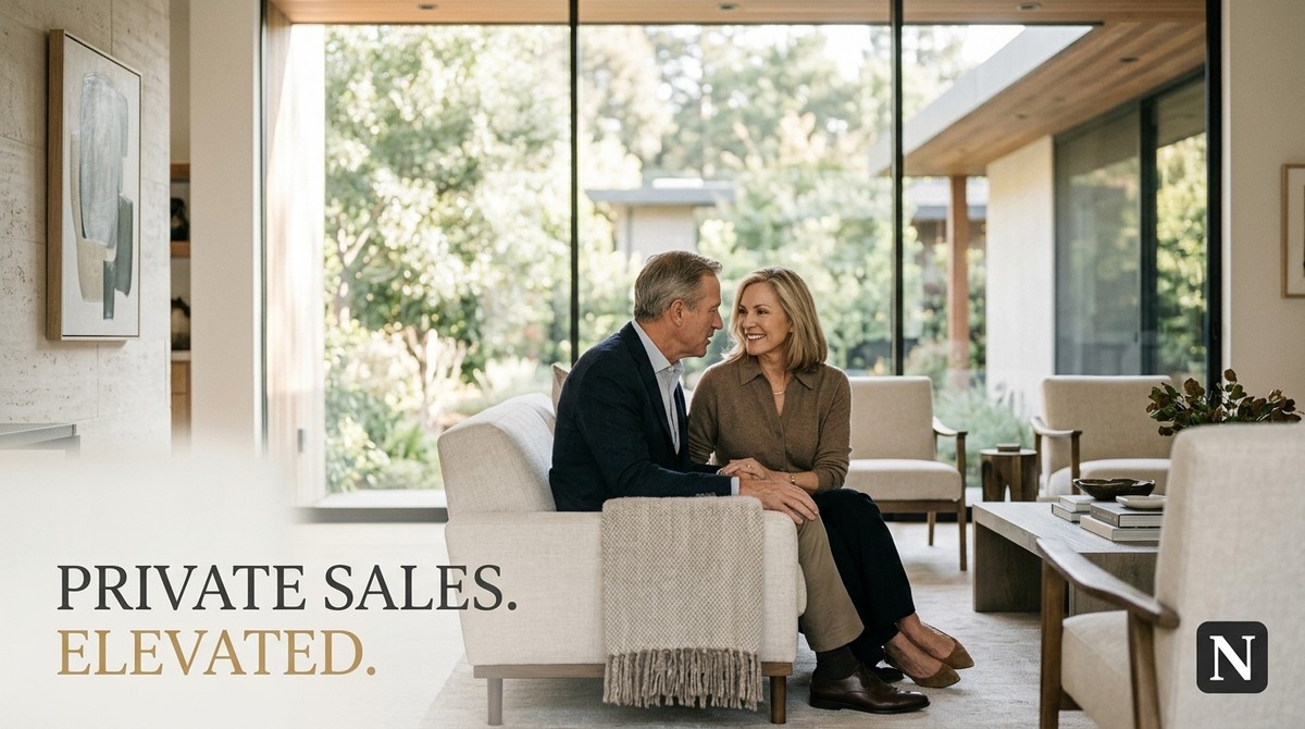 A couple sits on a sofa in a modern living room with large windows overlooking a lush garden.